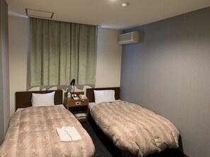 Una habitación de hotel con dos camas, una mesita de noche con lámpara, teléfono y una pequeña mesa.