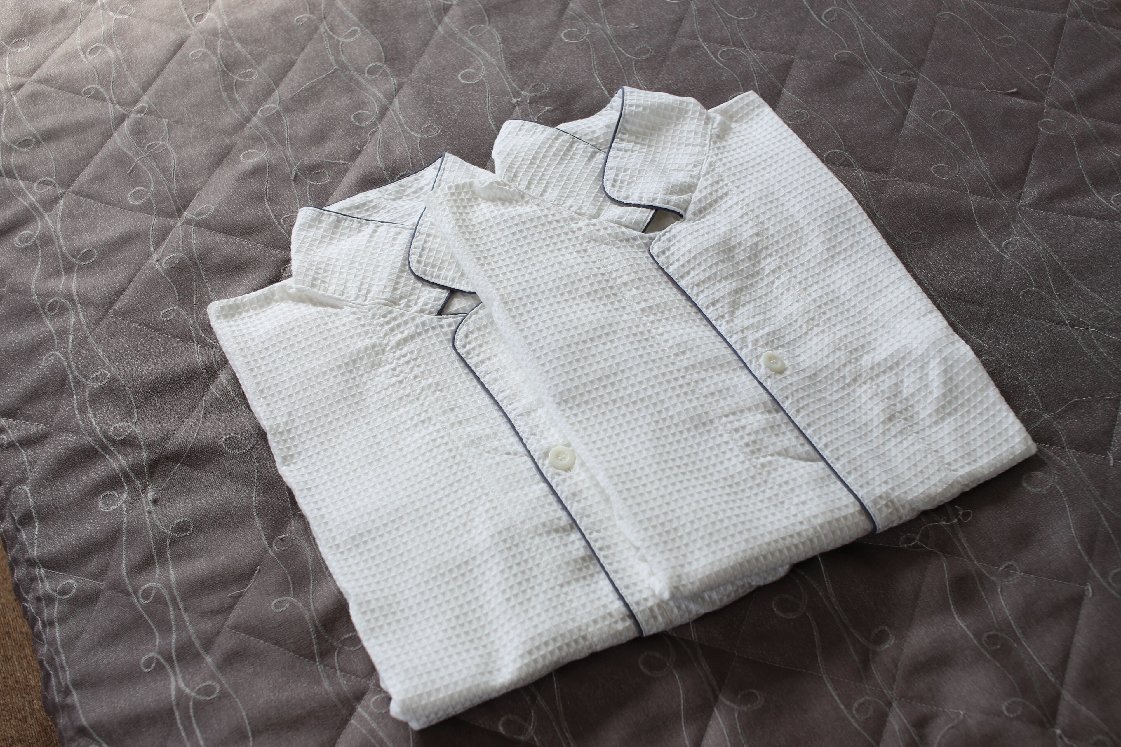 A neatly folded white shirt on a textured bedspread with a subtle pattern.