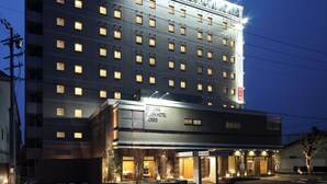 A multi-story hotel with a prominent sign, a ground-level entrance, and a parking lot. - Toyooka Green Hotel Morris (Toyooka)