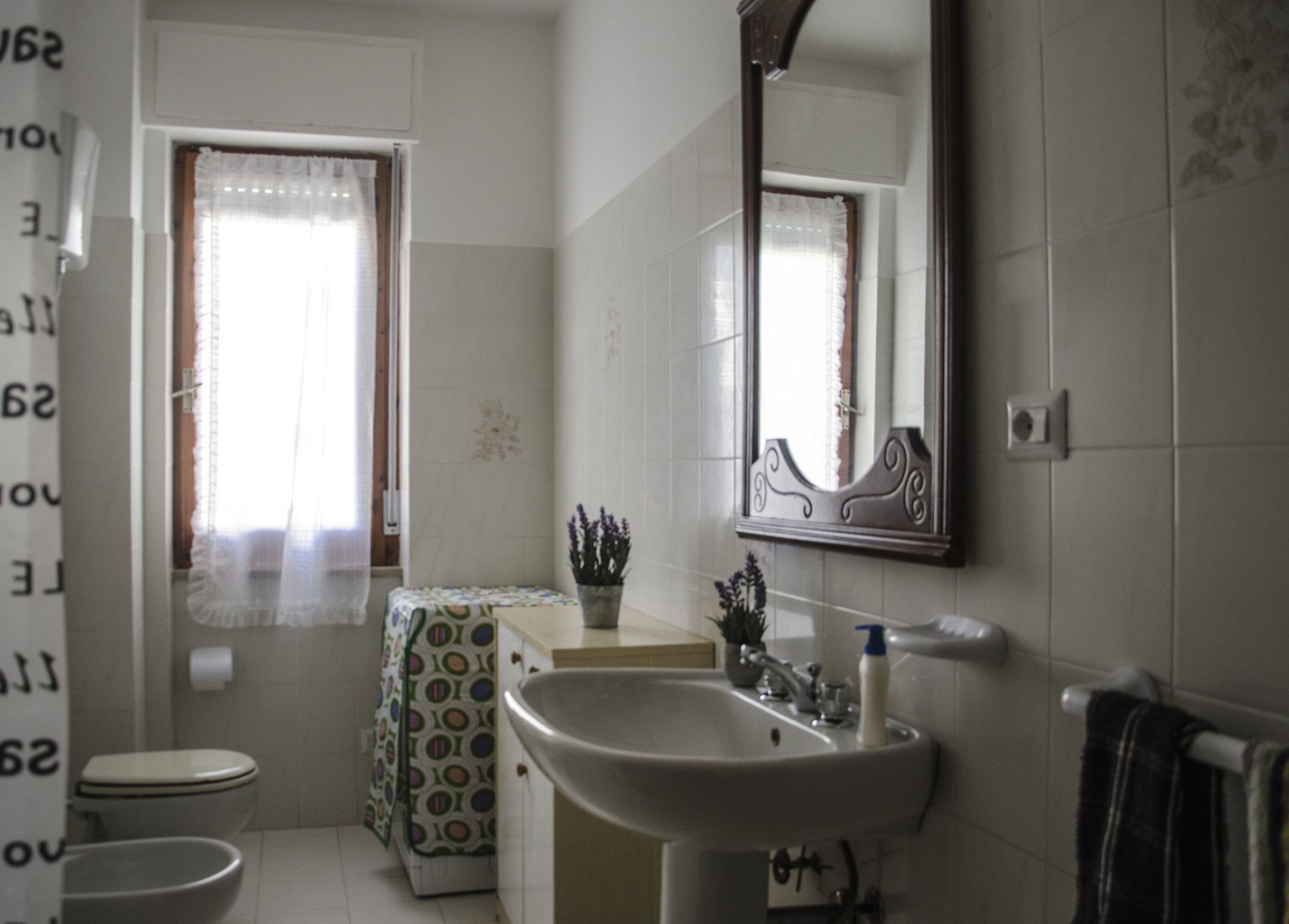 A bathroom with a toilet, sink, mirror, and a window with curtains.