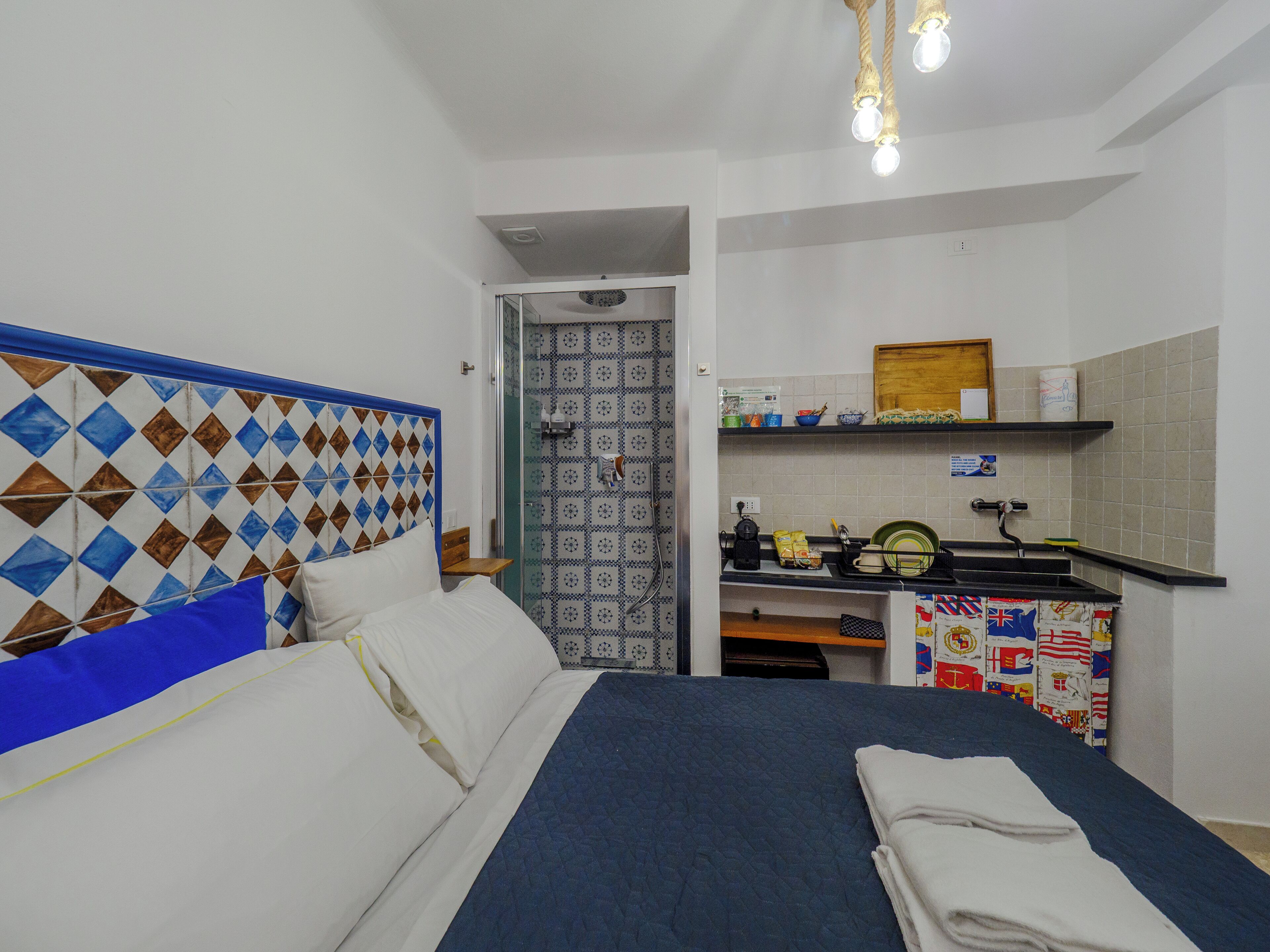 Een slaapkamer met een bed, een badkamer met douche, en een kitchenette met een gootsteen en fornuis.