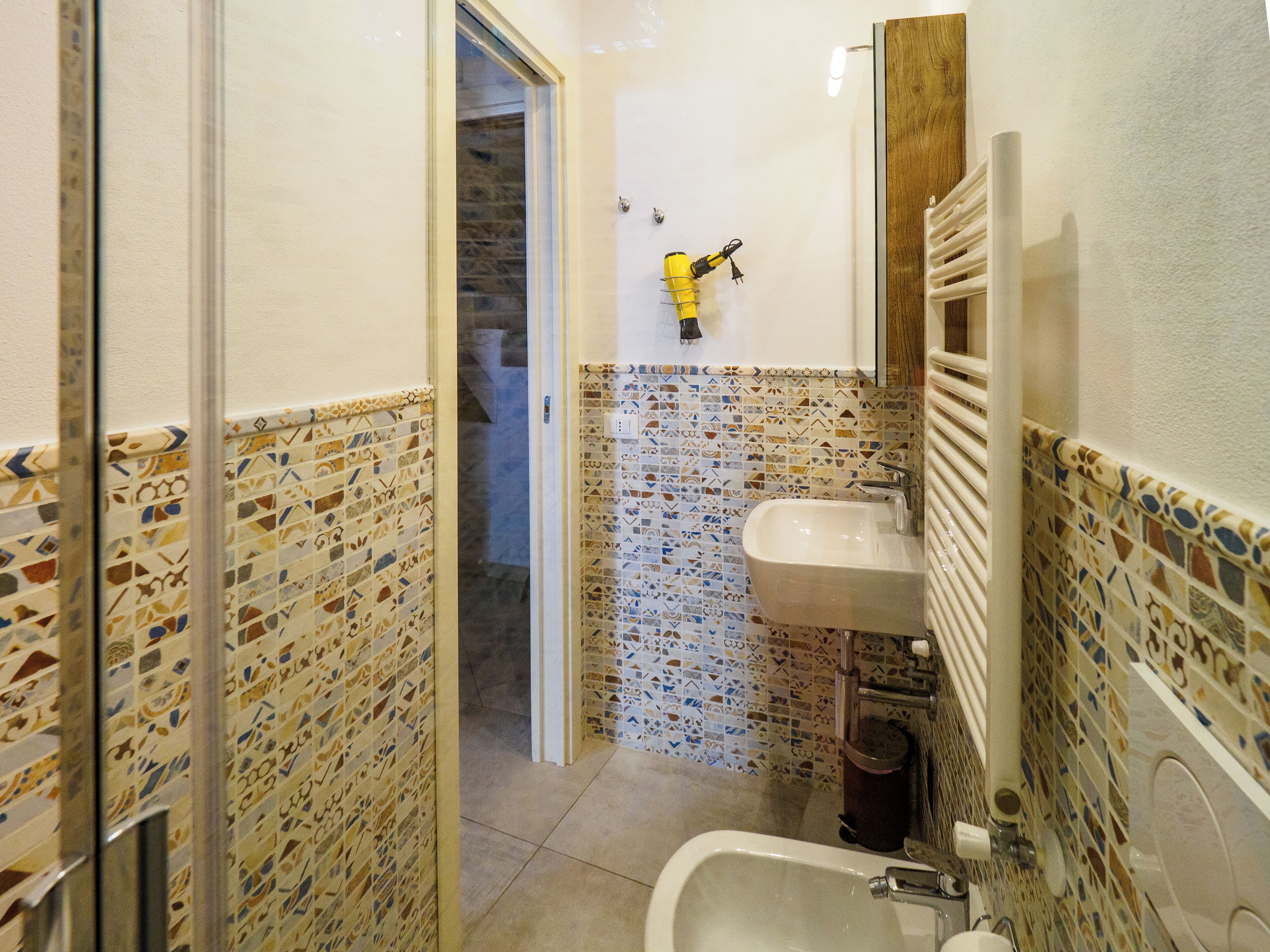 A bathroom with mosaic tile walls, a sink, and a toilet.