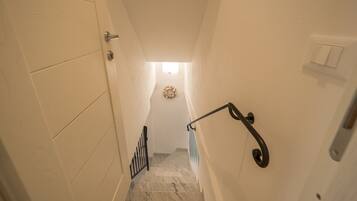 Un escalier étroit avec une main courante, une porte à gauche et un interrupteur à droite.