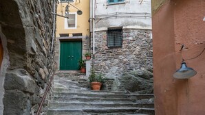 Una estrecha escalera de piedra conduce a una puerta verde, flanqueada por edificios con paredes de piedra y una lámpara de metal.