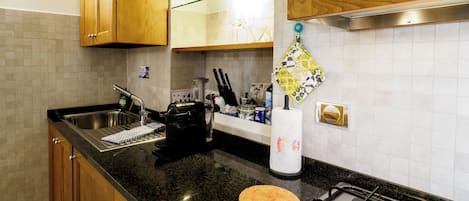 Une cuisine dotée de meubles en bois, d’un évier en acier inoxydable, d’une cuisinière à gaz et d’un plan de travail sur lequel sont disposés divers ustensiles de cuisine.