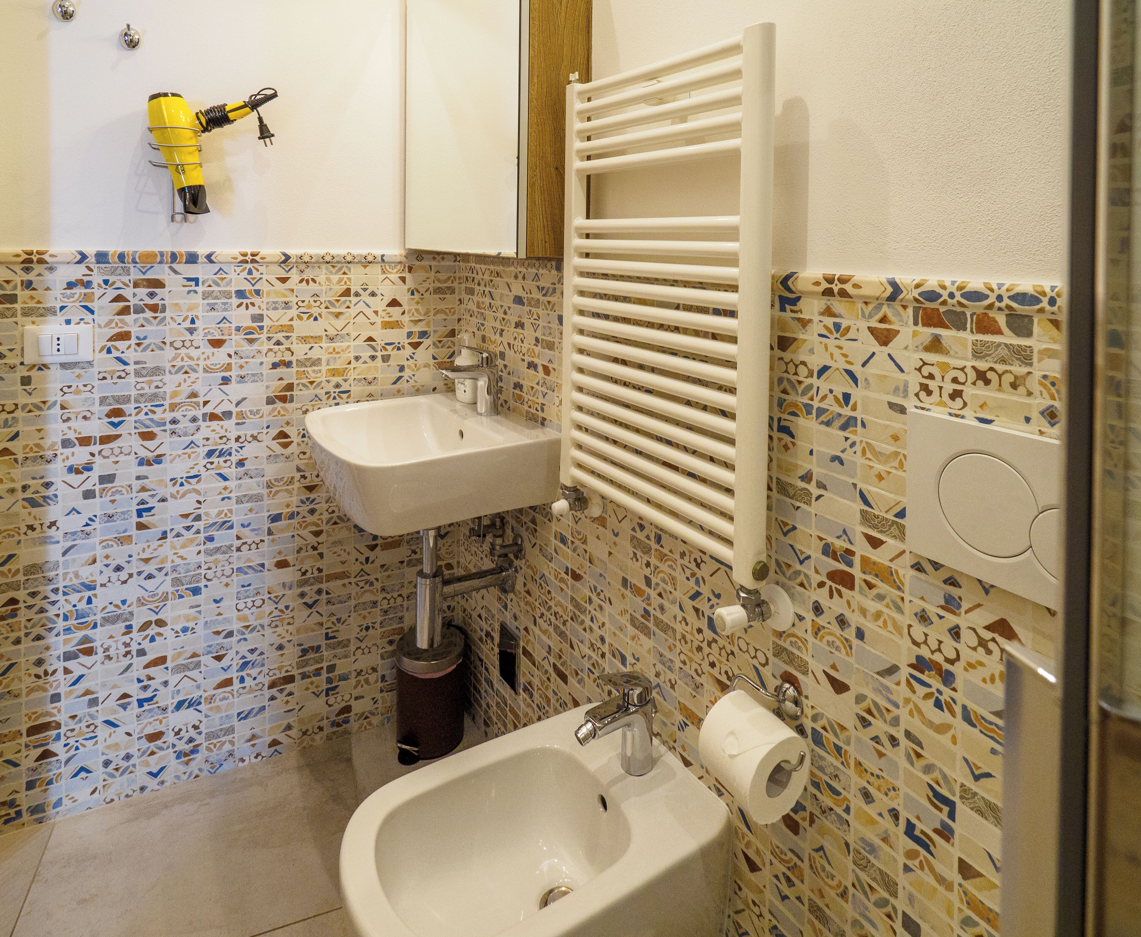Un baño con salpicadero de mosaicos, un lavamanos, un bidé y un perchero para toallas.