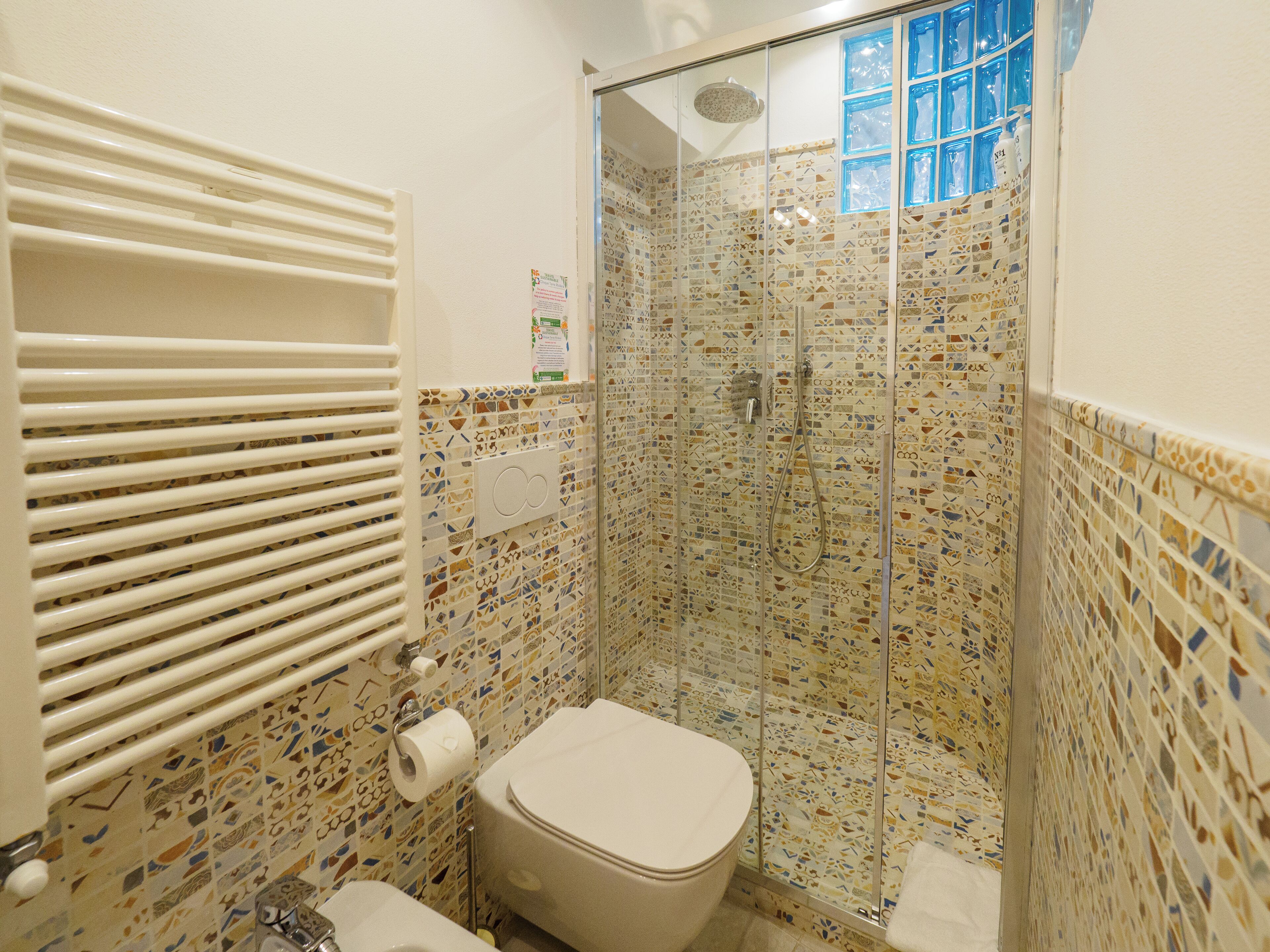 Et badeværelse med toilet, brusebad og mønstrede fliser.