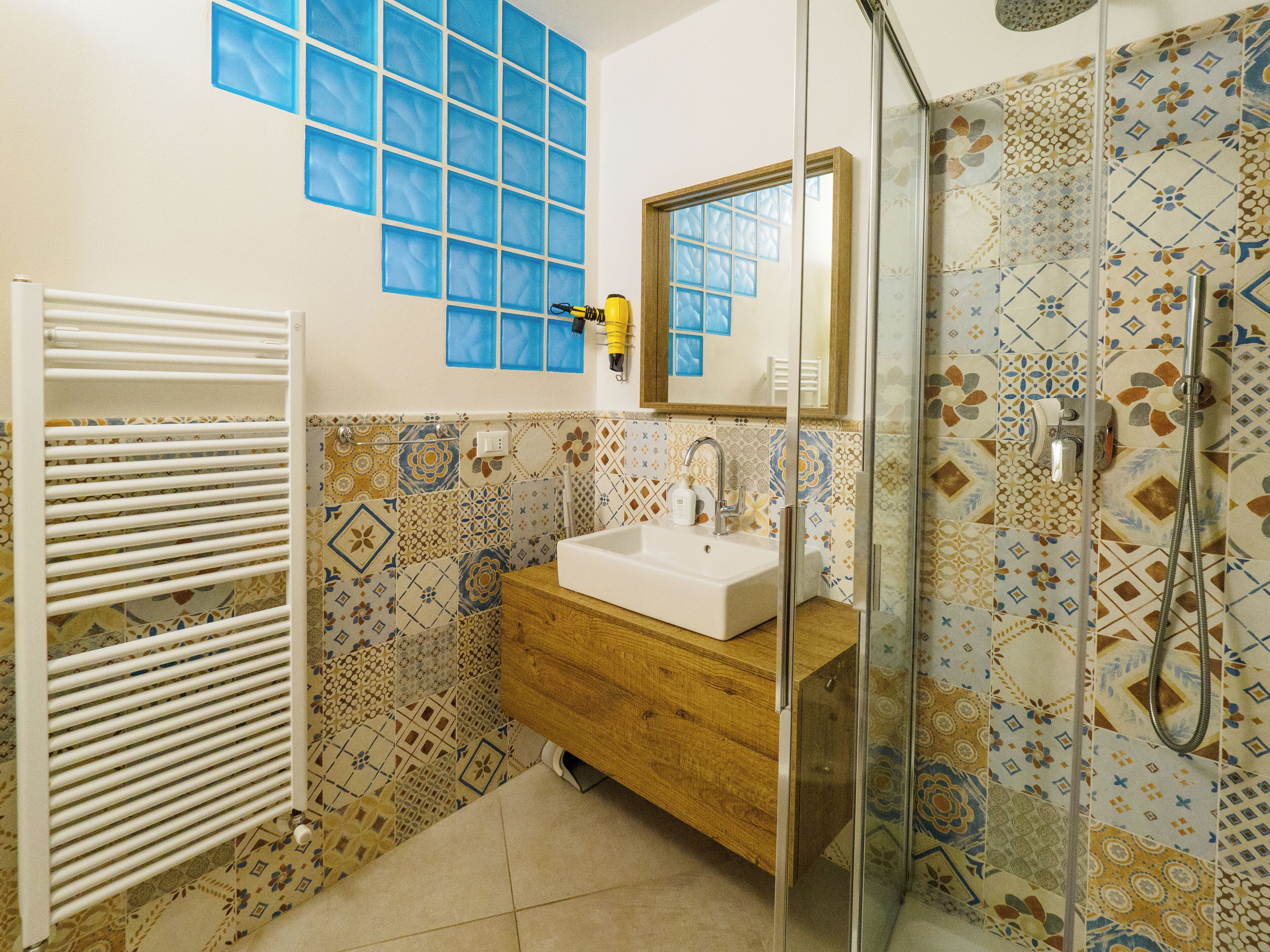 Un bagno con lavandino bianco, mobile bagno in legno e cabina doccia in vetro.