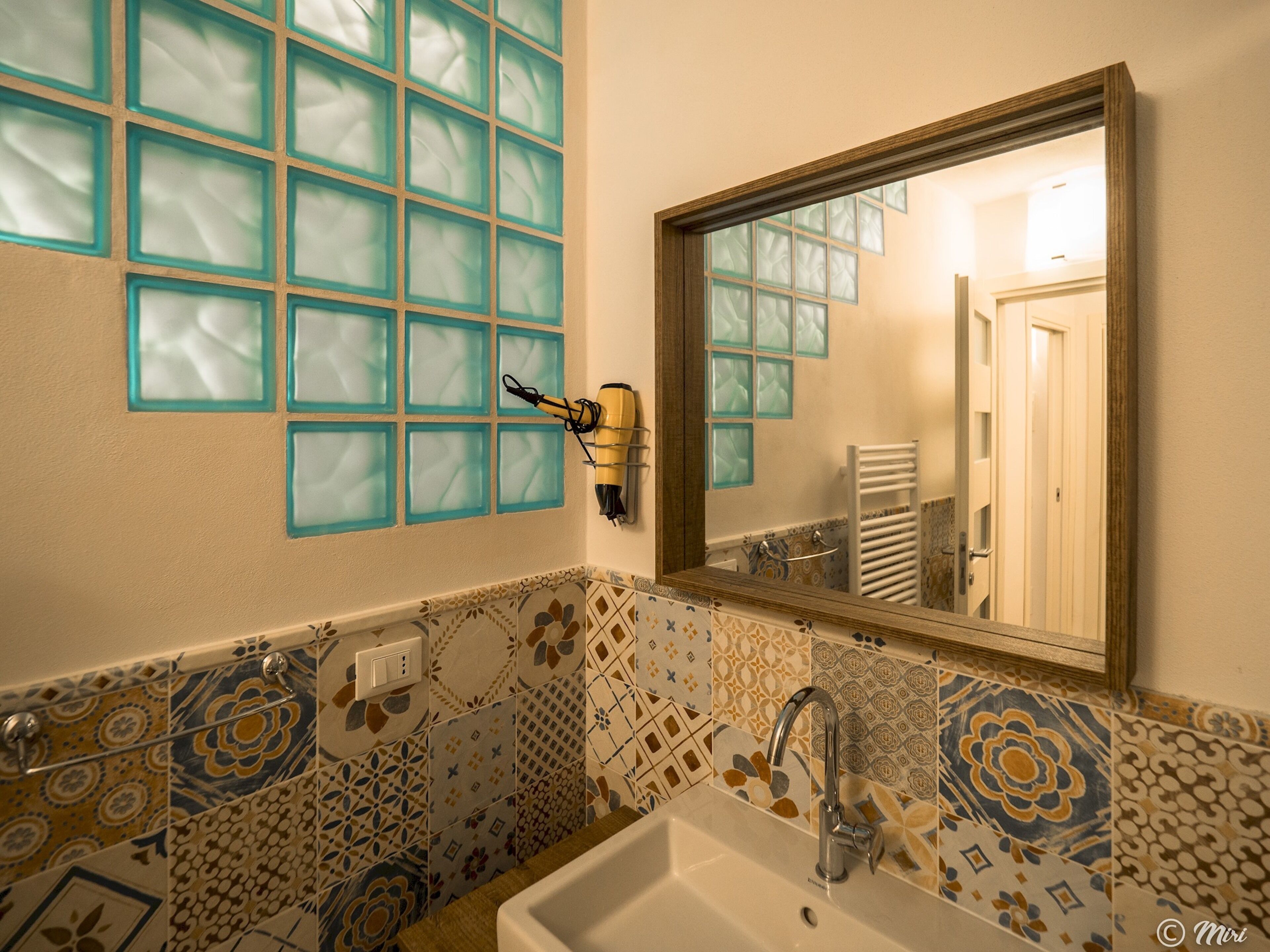 Een badkamer met een wastafel, spiegel en een aan de muur bevestigde haardroger.