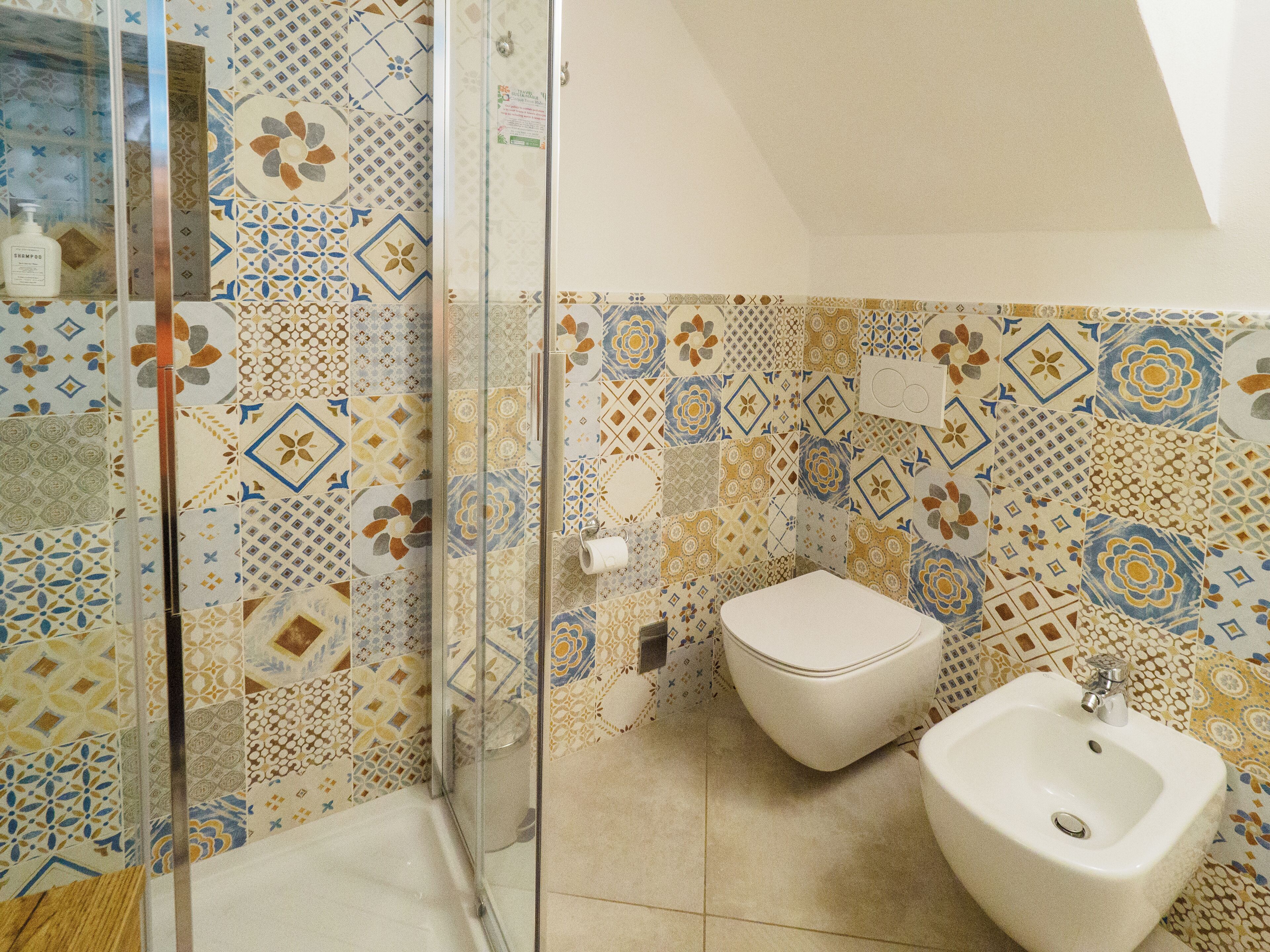 A bathroom with a shower, toilet, and bidet. The walls are decorated with patterned tiles.
