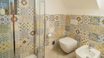 A bathroom with a shower, toilet, and bidet. The walls are decorated with patterned tiles.