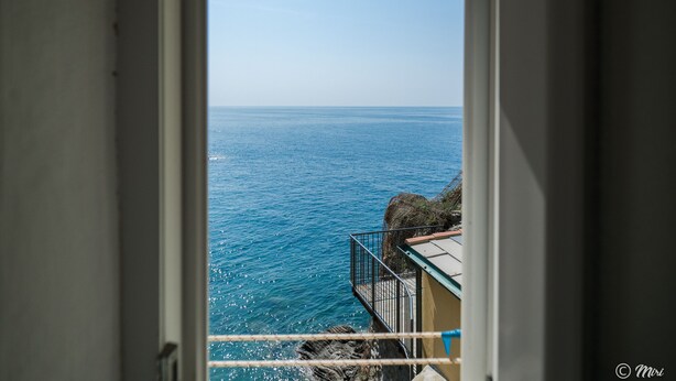 Vista del mar a través de una puerta abierta, con un balcón y un edificio a la vista.