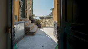 Un estrecho pasillo exterior con escalones de piedra que conducen a un balcón, plantas en macetas y vistas al mar.
