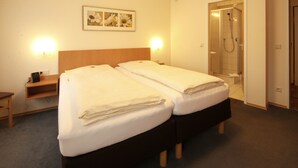 Una habitación de hotel con dos camas, ducha, mesita de noche y un cuadro colgado en la pared.