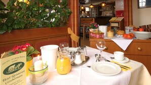 Una escena de desayuno con una mesa para dos personas, incluyendo platos, cubiertos, una vela y una jarra de jugo de naranja.