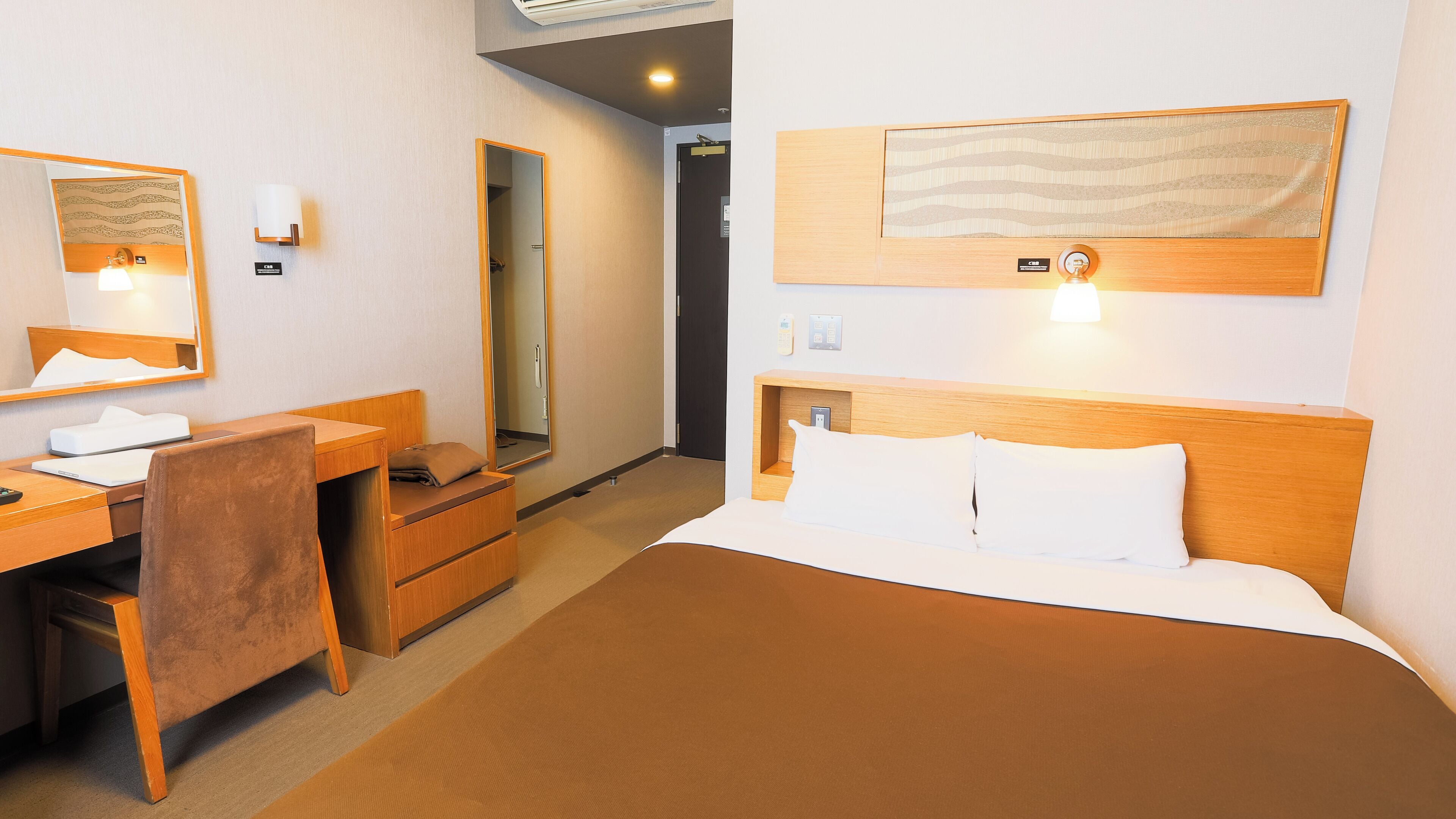 A hotel room with a bed, a desk, a chair, a mirror, and a wall-mounted artwork.