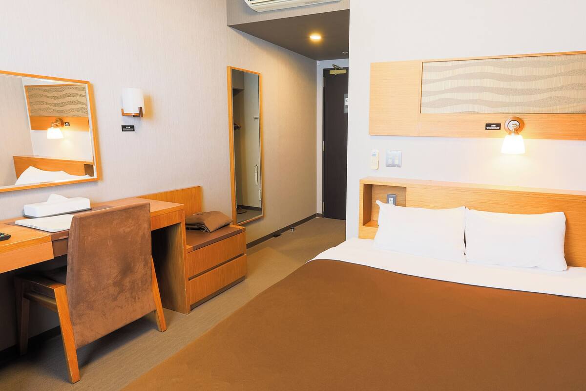 Hotellihuone, jossa on sänky, työpöytä, tuoli, peili ja seinälle kiinnitetty taideteos.