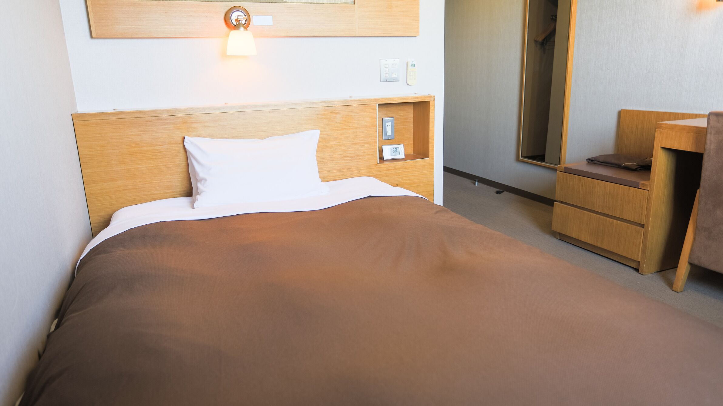 A hotel room with a bed, bedside table, nightstand, lamp, and a mirror.