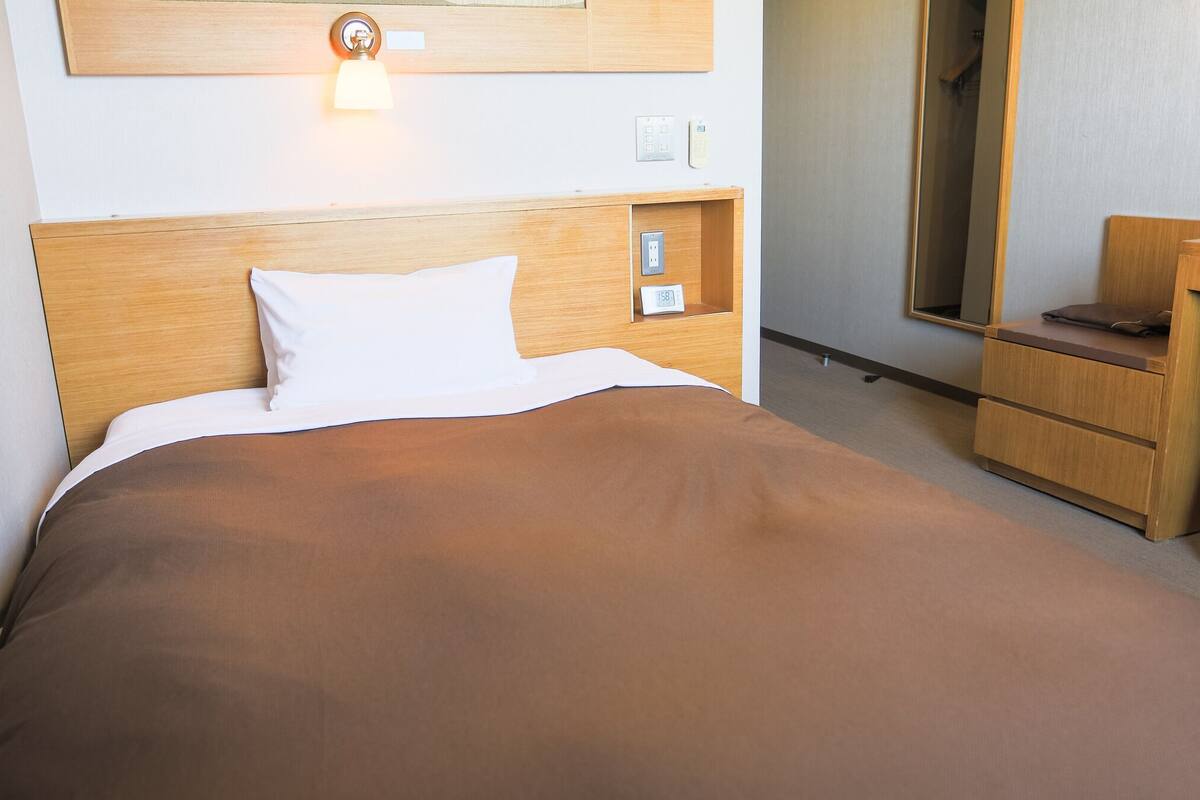 Hotellihuone, jossa on sänky, yöpöytä, lamppu ja peili.