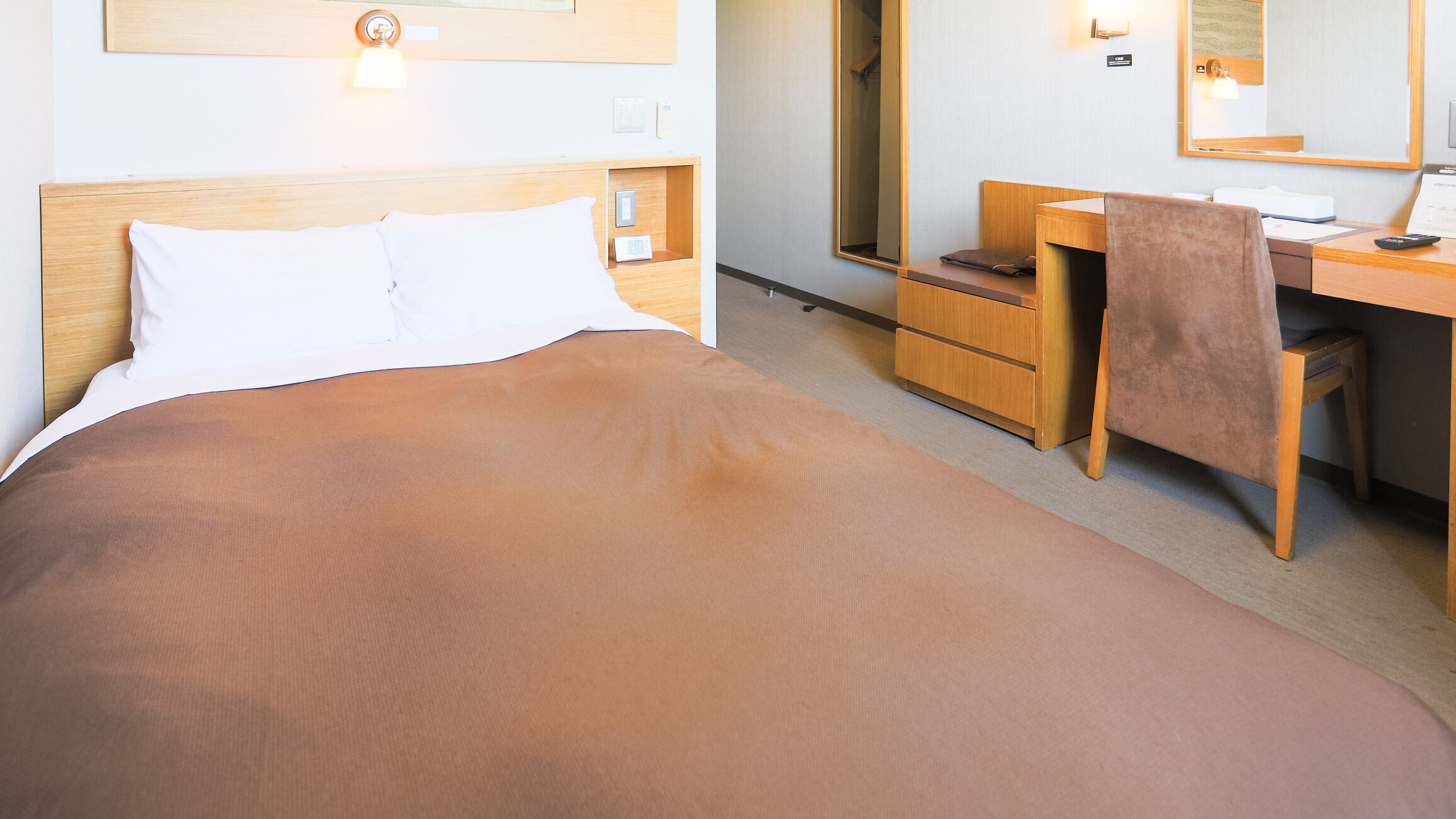 A hotel room with a bed, a desk, a chair, and a mirror.