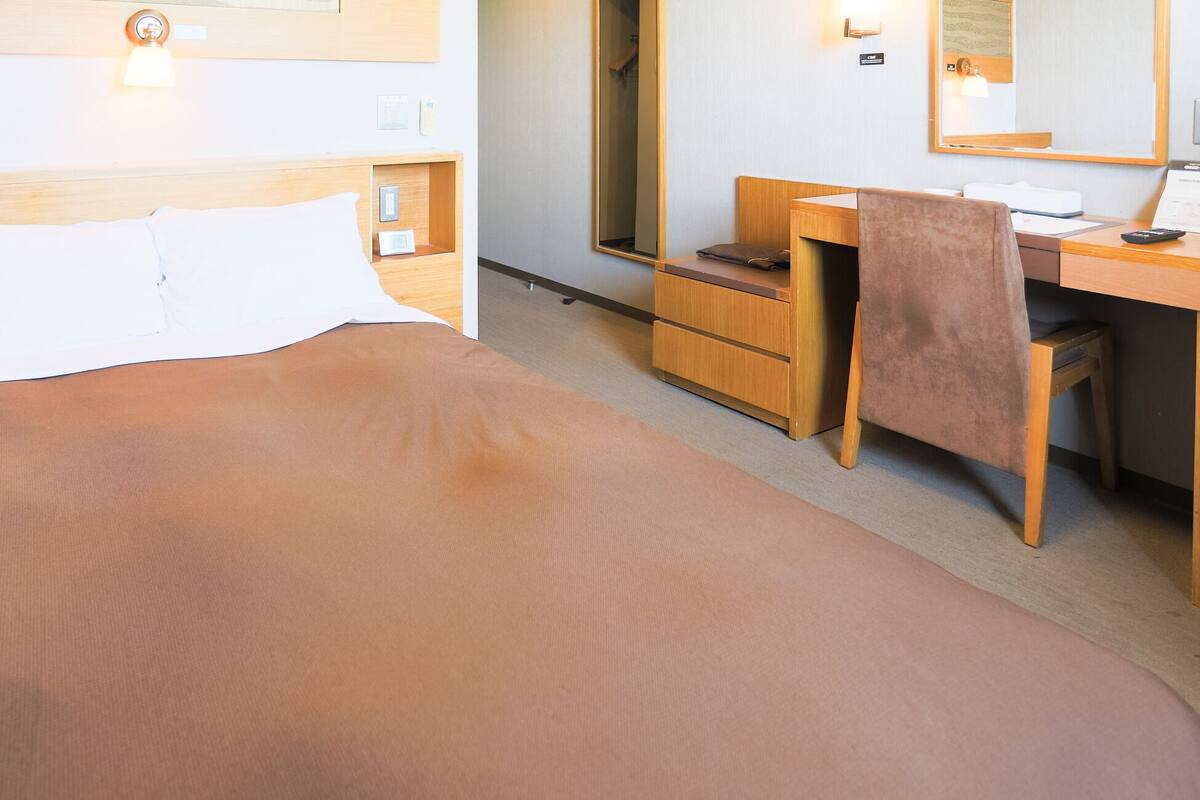 Hotellihuone, jossa on sänky, työpöytä, tuoli ja peili.