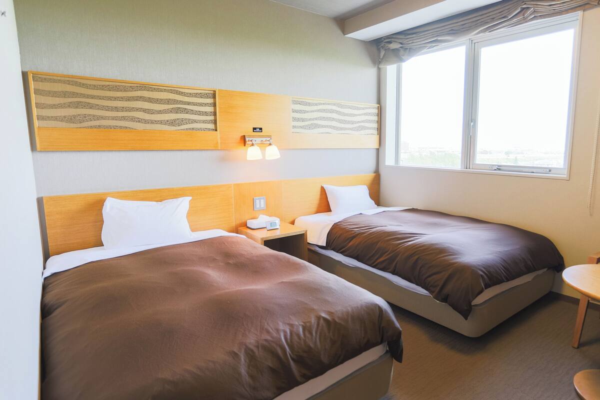 Hotellihuone, jossa on kaksi sänkyä, pieni pöytä ja ikkuna, josta on näkymä.