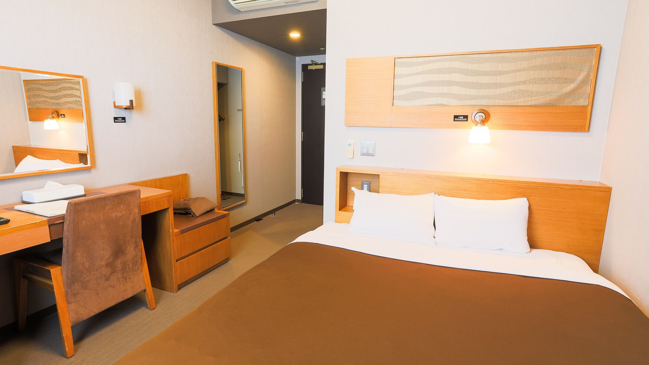 A hotel room with a bed, a desk, a chair, a mirror, and a wall-mounted artwork.