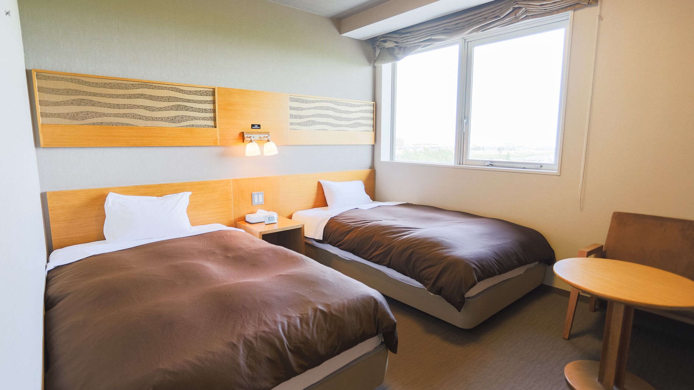 A hotel room with two beds, a small table, and a window.