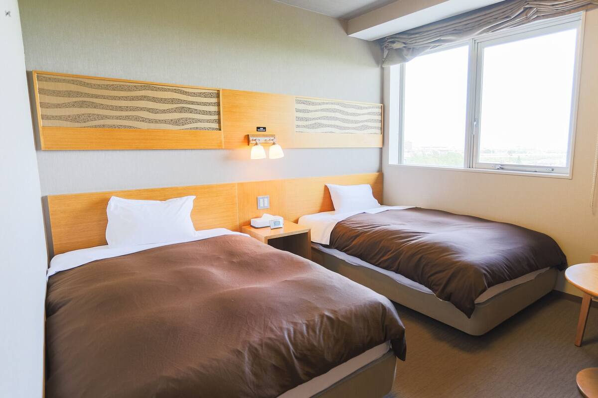 Hotellihuone, jossa on kaksi sänkyä, pieni pöytä ja ikkuna.