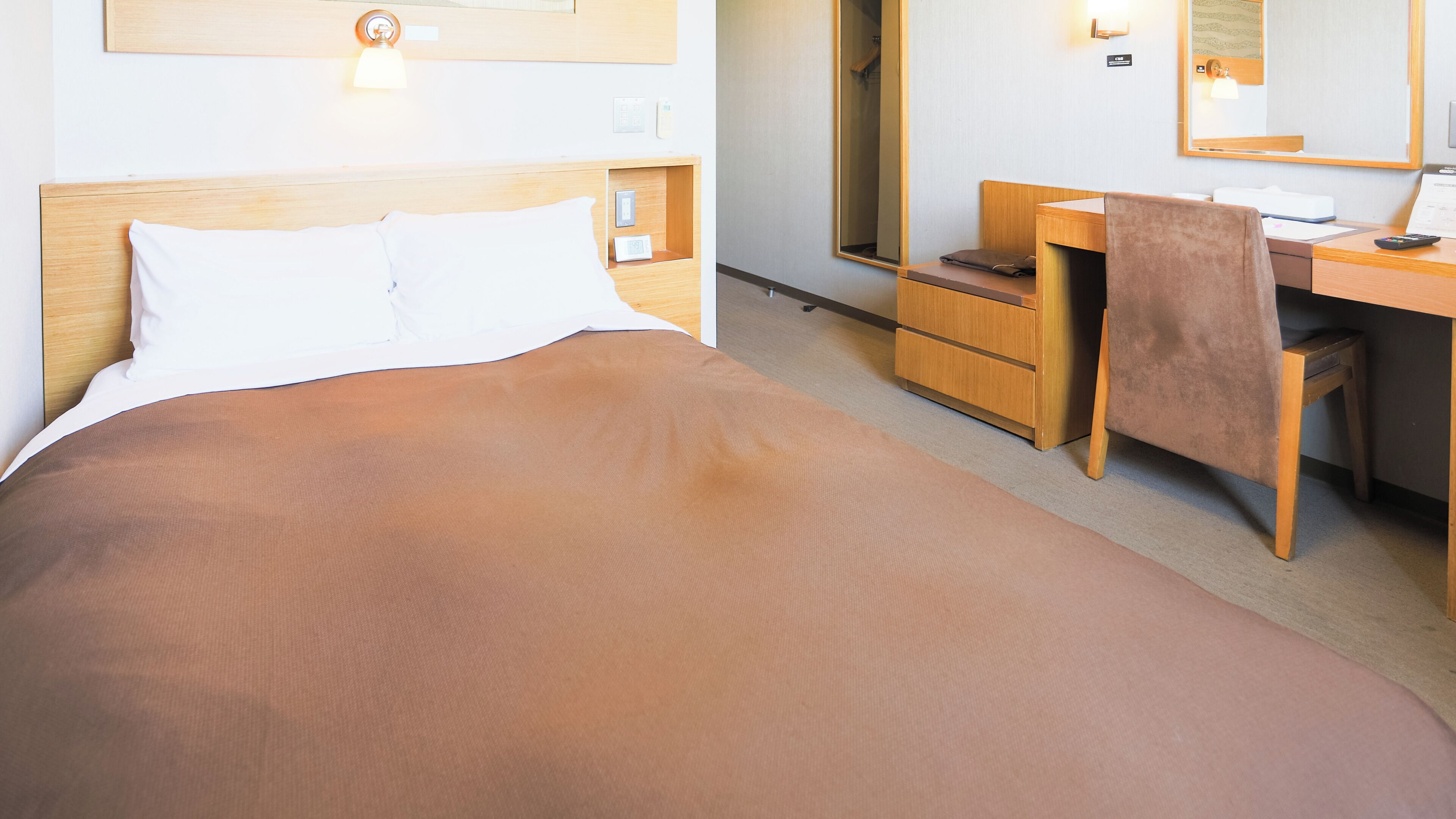 A hotel room with a bed, a desk, a chair, a mirror, and a wardrobe.