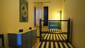 A small, single-bed room with a striped bedspread, a desk with a chair, a cabinet, and a wall-mounted lamp. - Casa Ostrica (Alghero)
