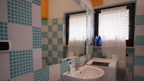 A bathroom with a white sink, mirror, and tiled walls. - Casa Ostrica (Alghero)