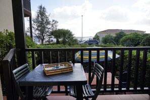 A balcony with a table and chairs, a striped umbrella, and a view of the sea and buildings in the background. - Casa Ostrica (Alghero)