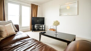 A modern living room with a leather sofa, a coffee table, a flat-screen TV, and a large window with curtains. - Beach Boulevard Apartment (Aberdeen)