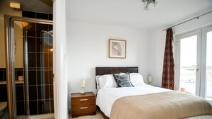 A bedroom with a bed, a nightstand, a framed picture, and a sliding glass door leading to a balcony. - Beach Boulevard Apartment (Aberdeen)