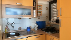 Una cocina con gabinetes amarillos, un lavamanos de acero inoxidable, una estufa y una silla azul.