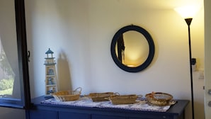 Una habitación con tocador, cestas de mimbre, una pequeña maqueta de faro y un espejo redondo en la pared.