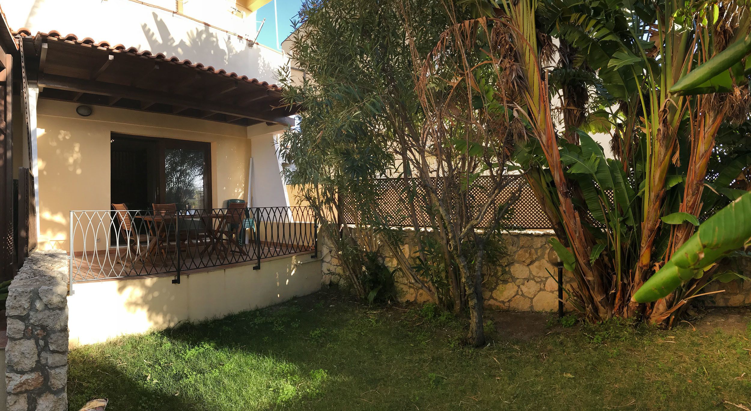 A house with a patio, a stone wall, and a garden with banana plants.