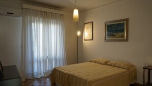 Un dormitorio con una cama, un escritorio, una lámpara de pie y dos cuadros en la pared.