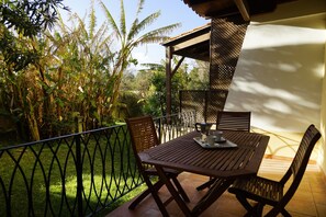 An outdoor patio with a wooden table and chairs, surrounded by a metal fence and lush greenery. - Casa Polpo (Alghero)