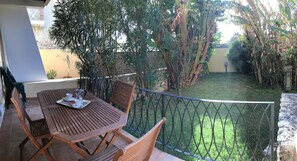 A wooden table and chairs on a balcony with a metal railing, overlooking a garden with various plants and a lawn.