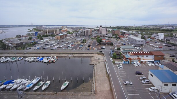 A marina with boats docked, a parking lot, and buildings in the background. - HOTEL CROWN HILLS TSUCHIURAEKIHIGASHI (Tsuchiura)