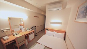 A hotel room with a bed, a desk, a chair, a mirror, a bedside table, and an air conditioning unit. - HOTEL CROWN HILLS TSUCHIURAEKIHIGASHI (Tsuchiura)