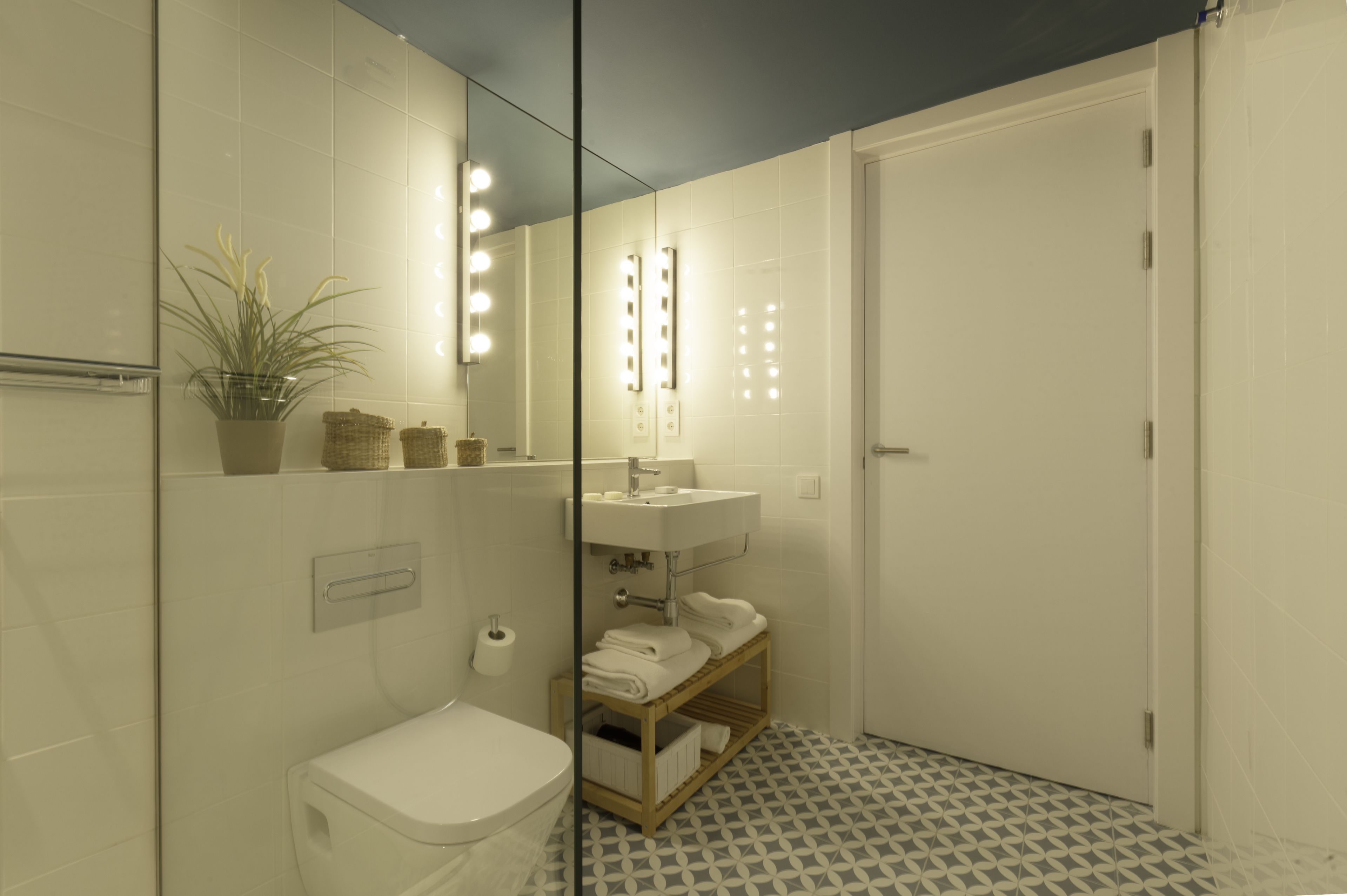 A bathroom with a toilet, sink, mirror with lights, and a patterned floor.