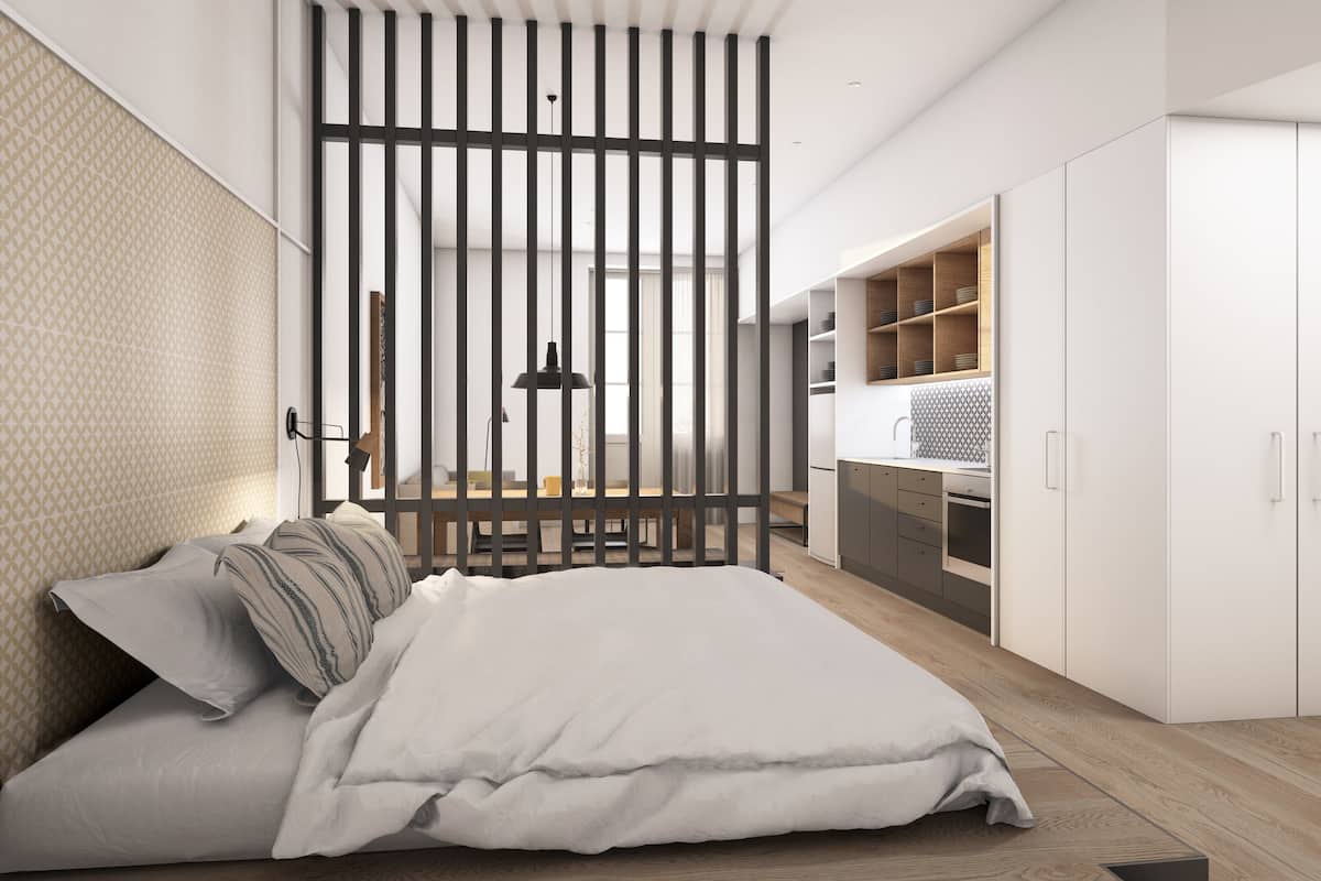 Un dormitorio moderno con una cama grande, un separador de madera y una kitchenette.