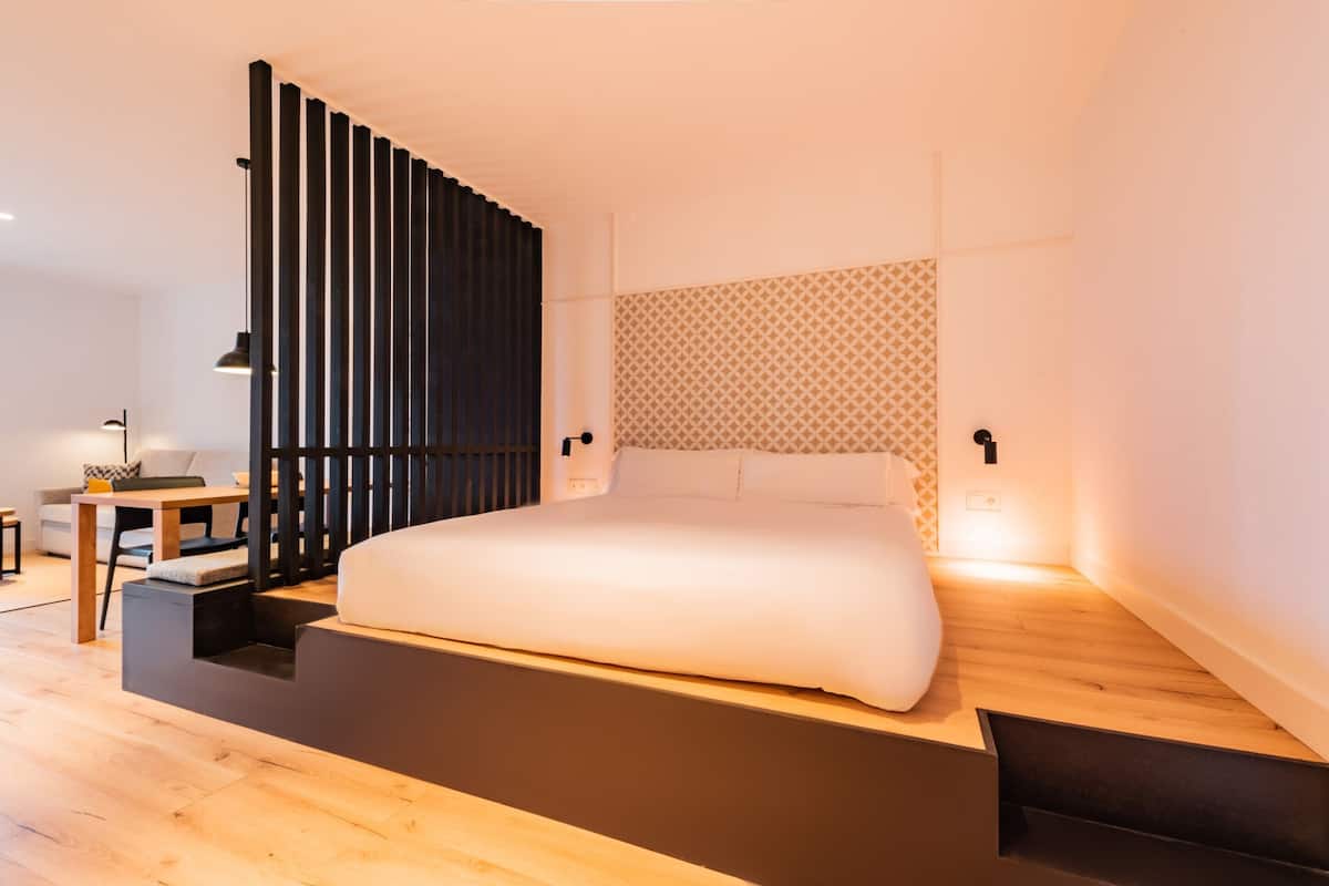 Un dormitorio moderno con una cama grande, suelo de madera, una pared divisoria negra y un papel tapiz estampado en la pared contigua.