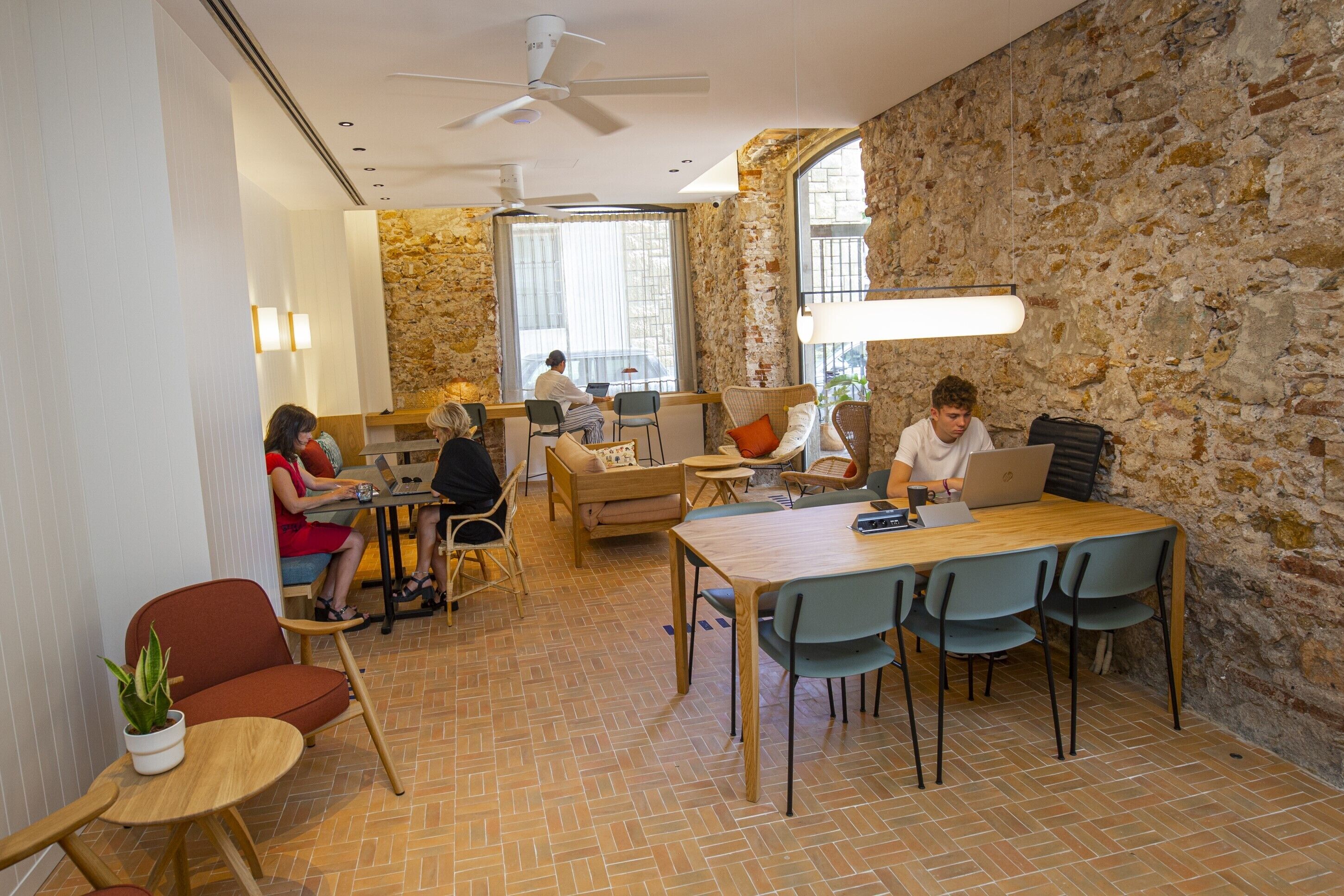 A modern co-working space with a stone wall, wooden furniture, and large windows.