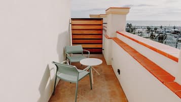 A balcony with two chairs and a small table, overlooking a marina with boats and palm trees.