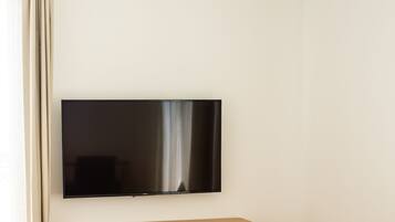 A modern living room with a flat-screen TV mounted on the wall, a wooden coffee table, a small wooden side table, a chair, and a desk with a chair.