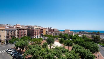 A coastal cityscape with historic buildings, a clear blue sky, and a parking area with cars.